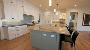 A modern kitchen with white cabinets, a large island, and a dining area with bar stools.