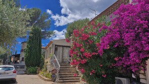 A building with a stone staircase leading to a door, surrounded by lush greenery and vibrant pink flowers. - Maison Provençale Familiale, Avec Jardin et Parking, 1, Proche Plage (Saint-Cyr-sur-Mer)
