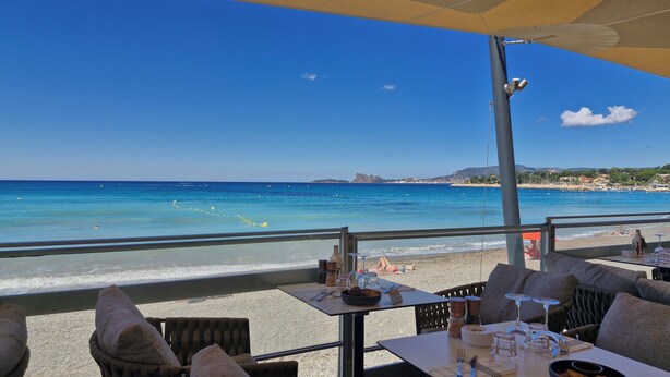 A beachside restaurant with outdoor seating overlooking the sea, featuring a table set with cutlery and a bottle. - Maison Provençale Familiale, Avec Jardin et Parking, 1, Proche Plage (Saint-Cyr-sur-Mer)