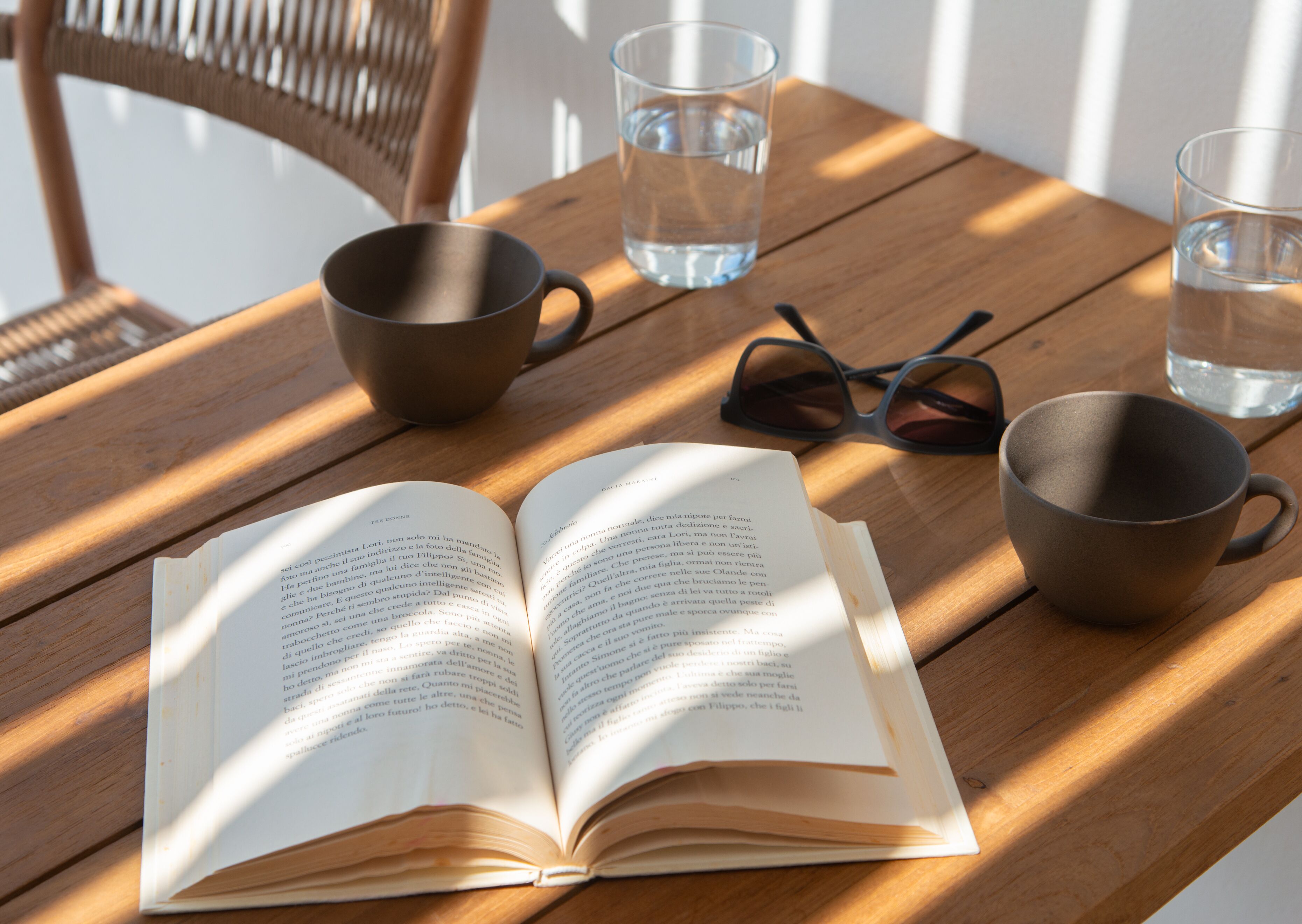 Un livre ouvert sur une table en bois, avec deux verres et une paire de lunettes de soleil.