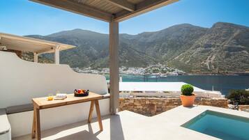 Una terraza con una mesa de madera, una planta en maceta y vistas a un paisaje montañoso y un cuerpo de agua.