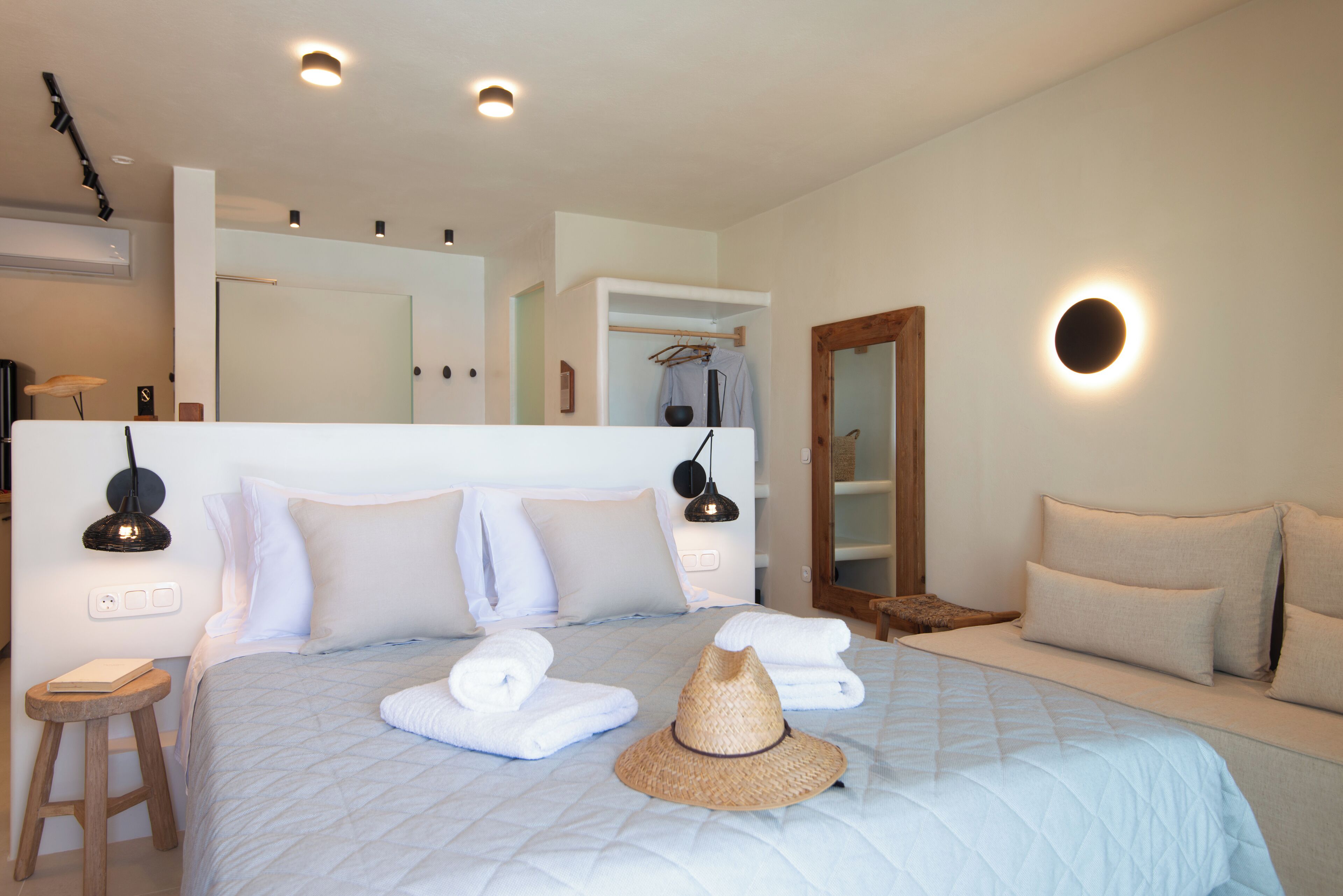A neatly made bed with towels and a straw hat, a bedside lamp, and a mirror above the bed.