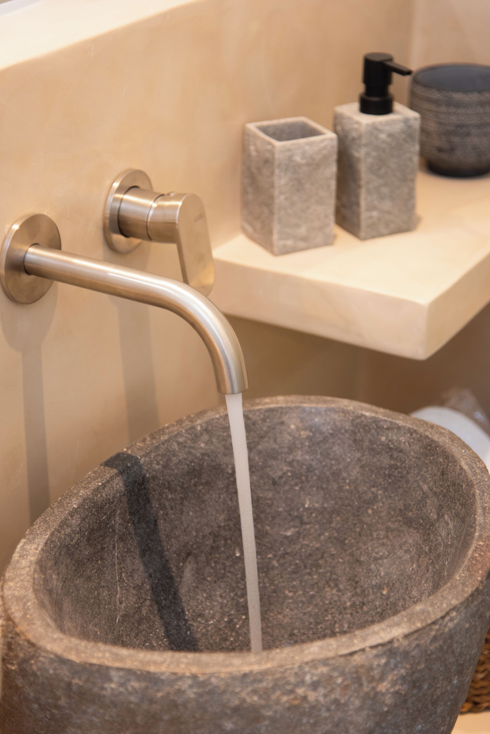 A stone basin with a faucet, a soap dispenser, and a container on a beige countertop.