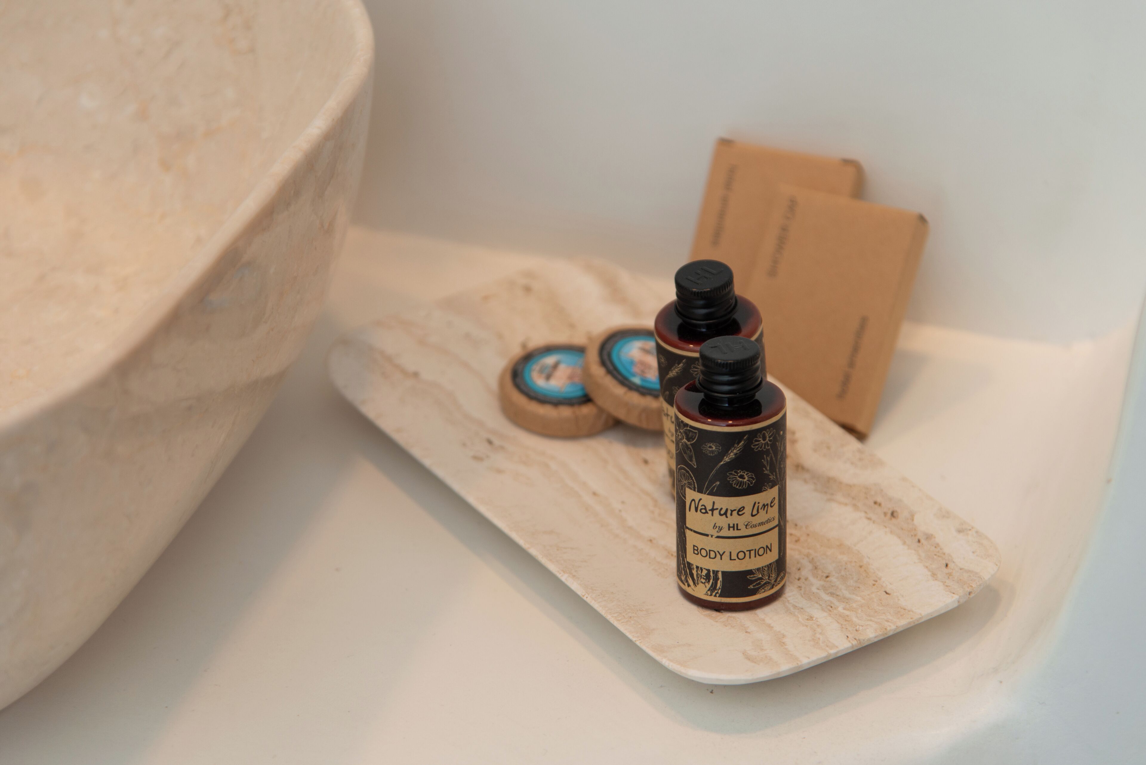 Une salle de bain avec une grande baignoire, une étagère en bois sur laquelle reposent deux flacons de lotion, et une boîte en bois.