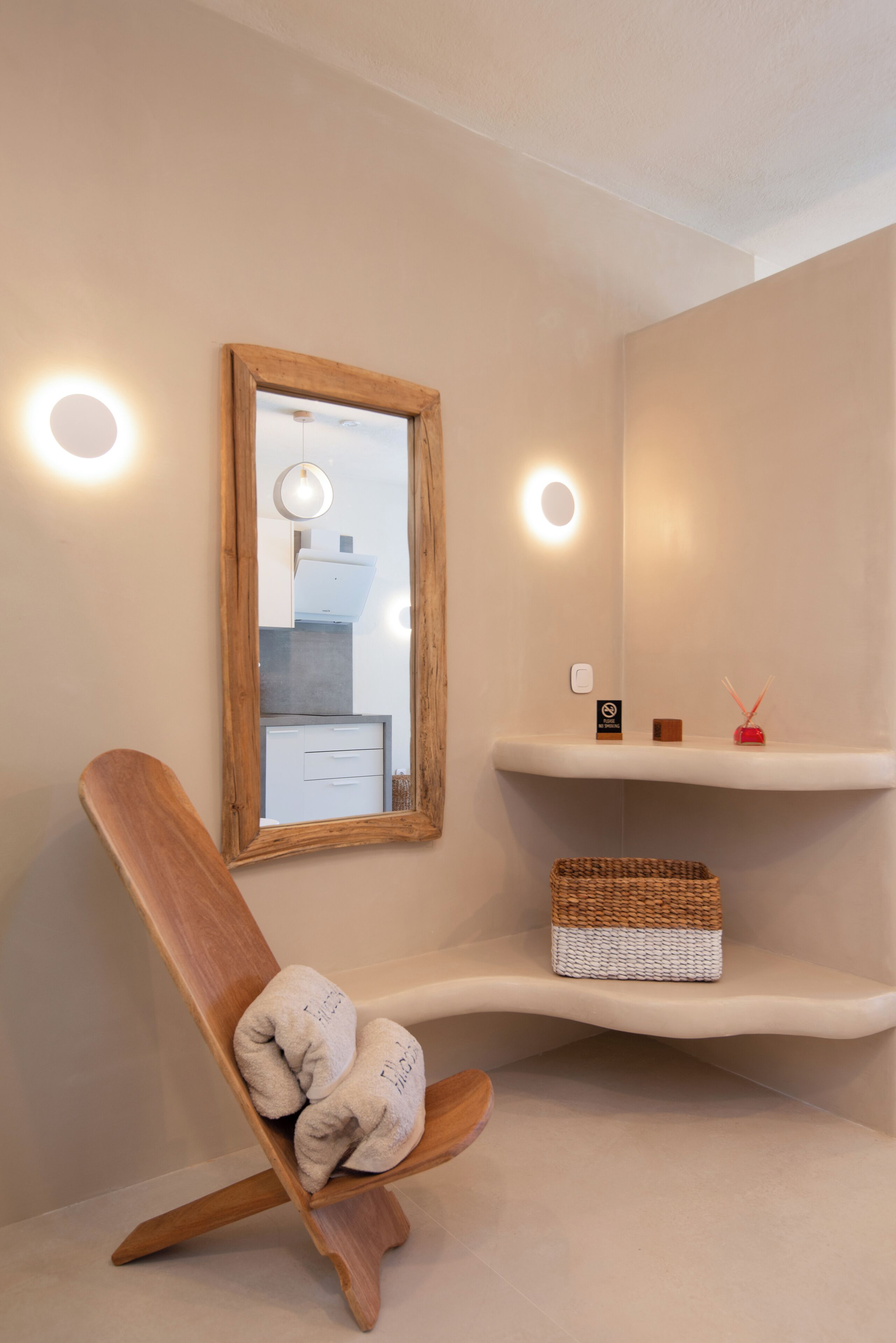 Un baño moderno con una silla de madera, un espejo y repisas con artículos de aseo.