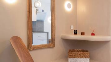 Un baño moderno con una silla de madera, un espejo y repisas con artículos de aseo.