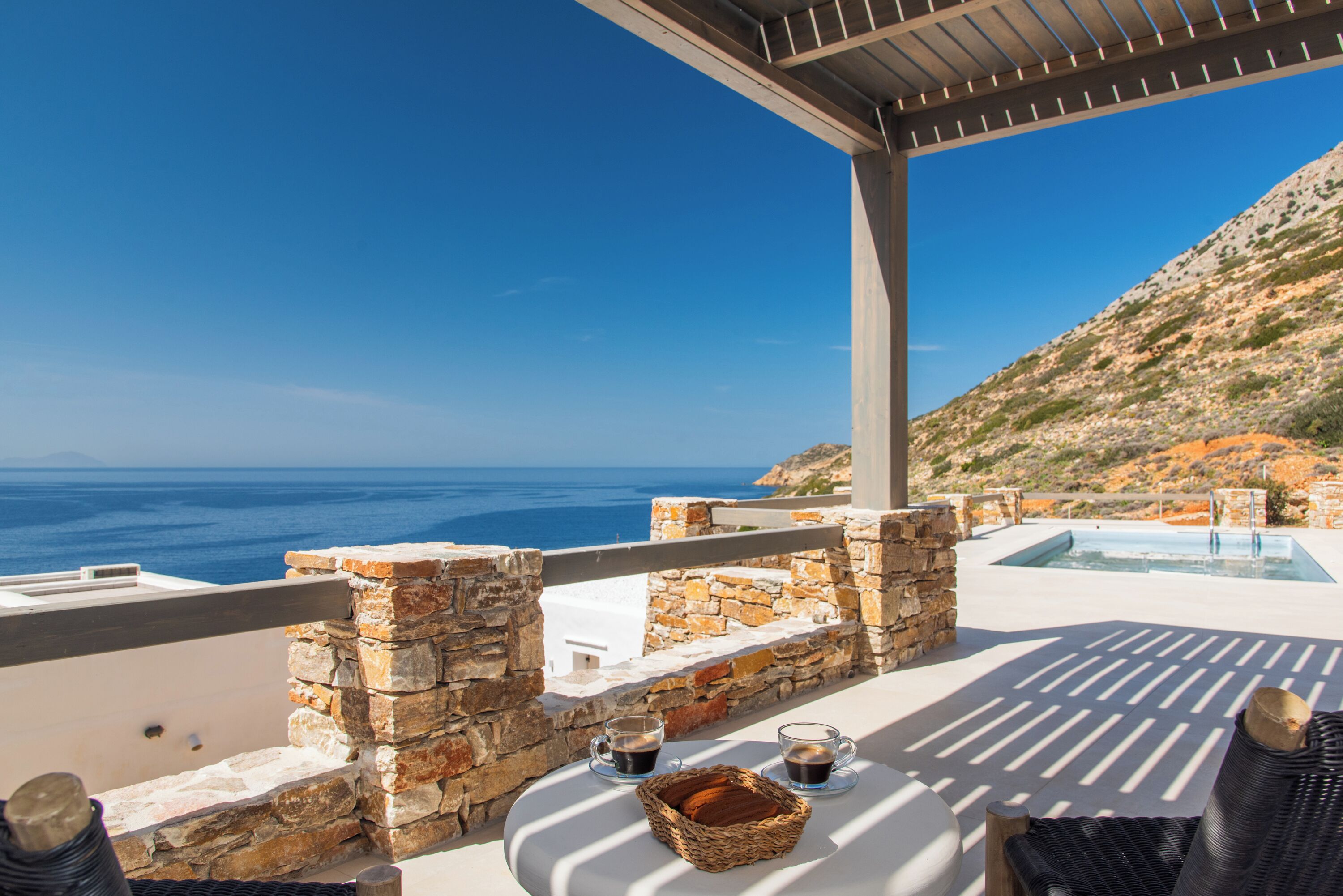 Una terraza con muros de piedra, una piscina y vistas al mar.