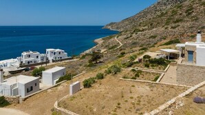 A coastal village with white buildings, a rocky hillside, and a clear blue sea. - Filadaki Villas (Sifnos)
