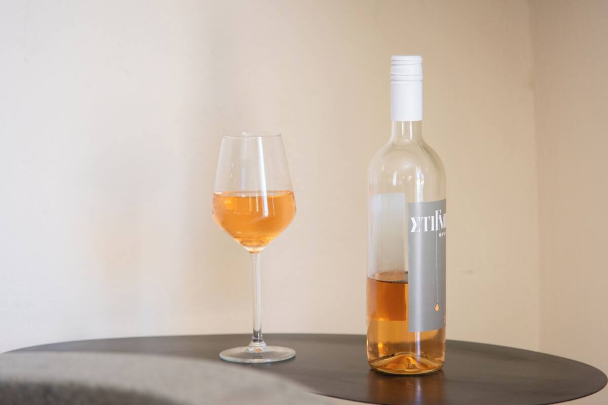 A bottle of wine and a glass on a round table against a plain wall.