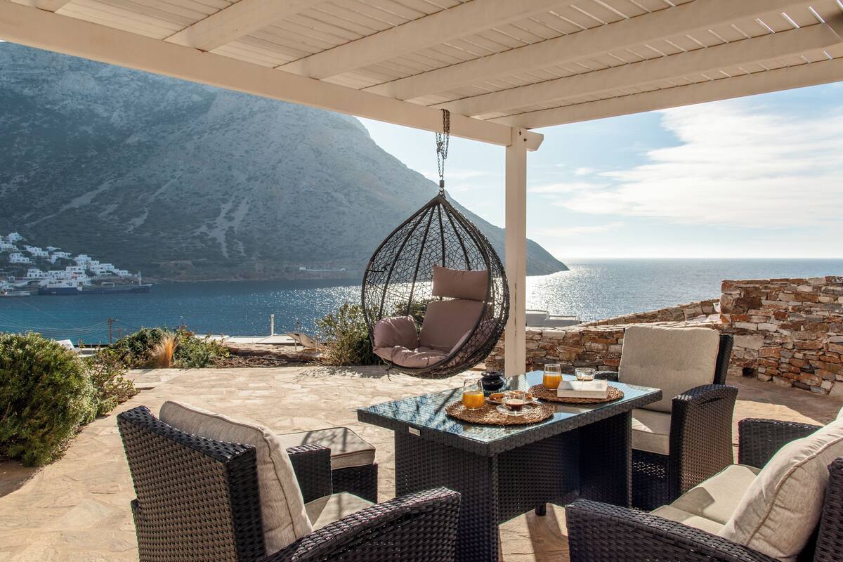 A patio with wicker furniture, a hanging chair, and a table set with drinks and snacks.