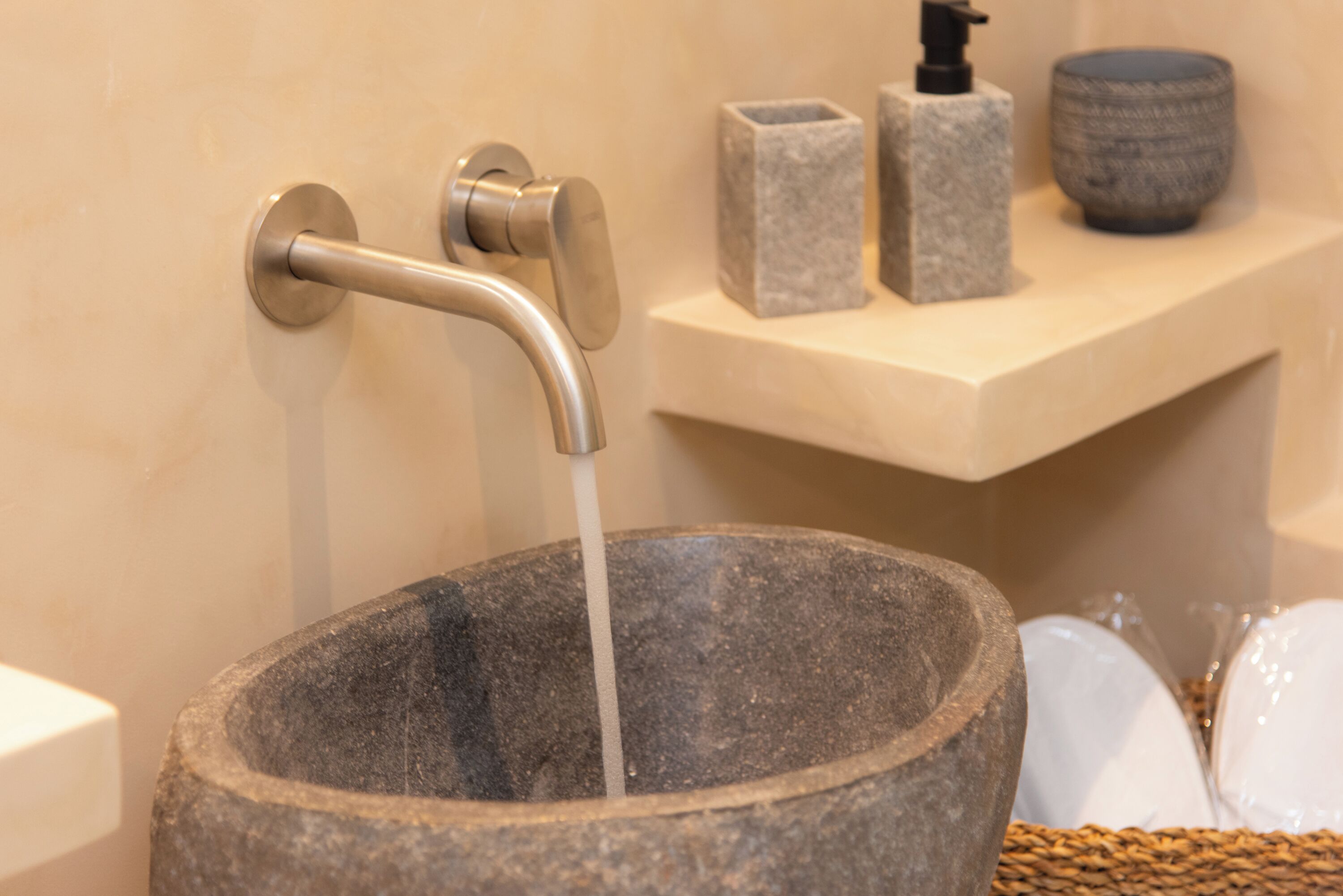 A stone basin with a faucet, a soap dispenser, and a decorative bowl on a shelf.