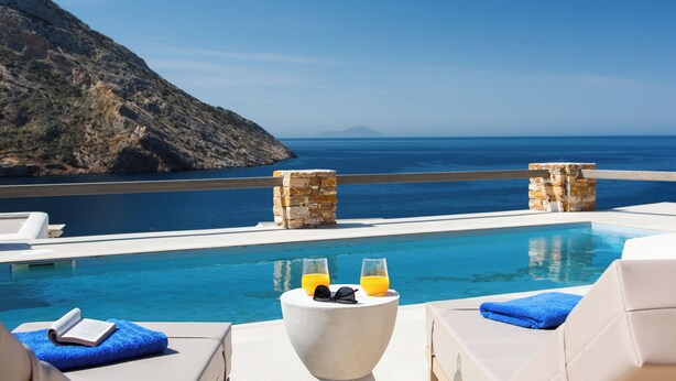 A poolside area with a view of the sea, a stone pillar, and a lounge chair. - Filadaki Villas (Sifnos)