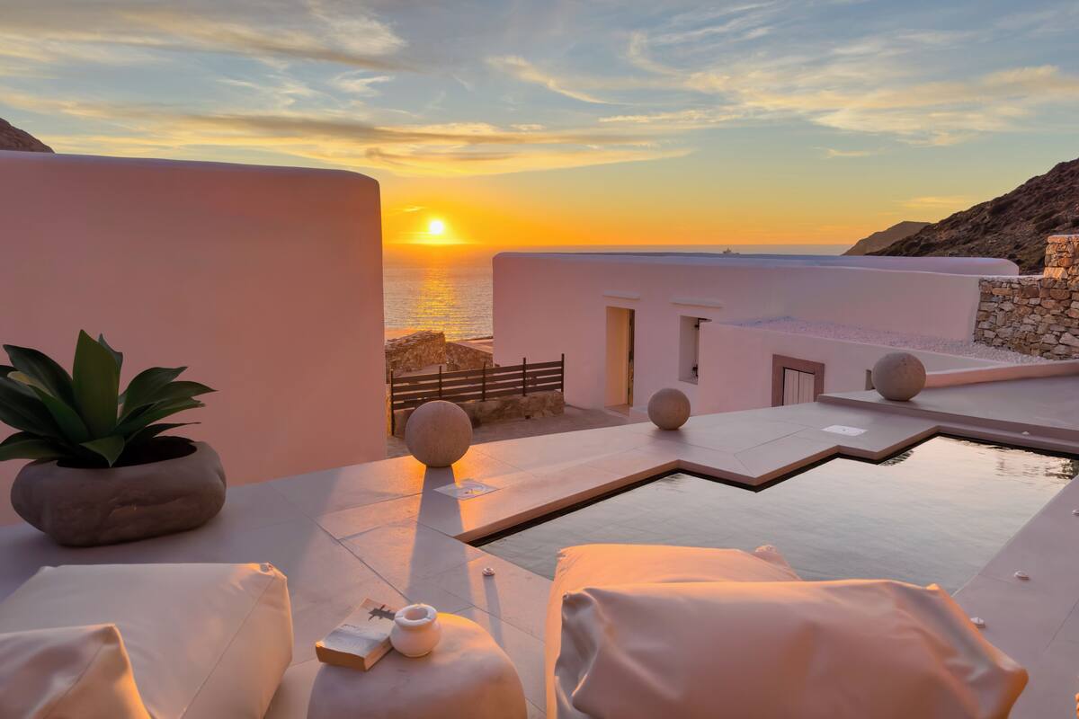 A serene rooftop pool area with a sunset view, white walls, and a potted plant.