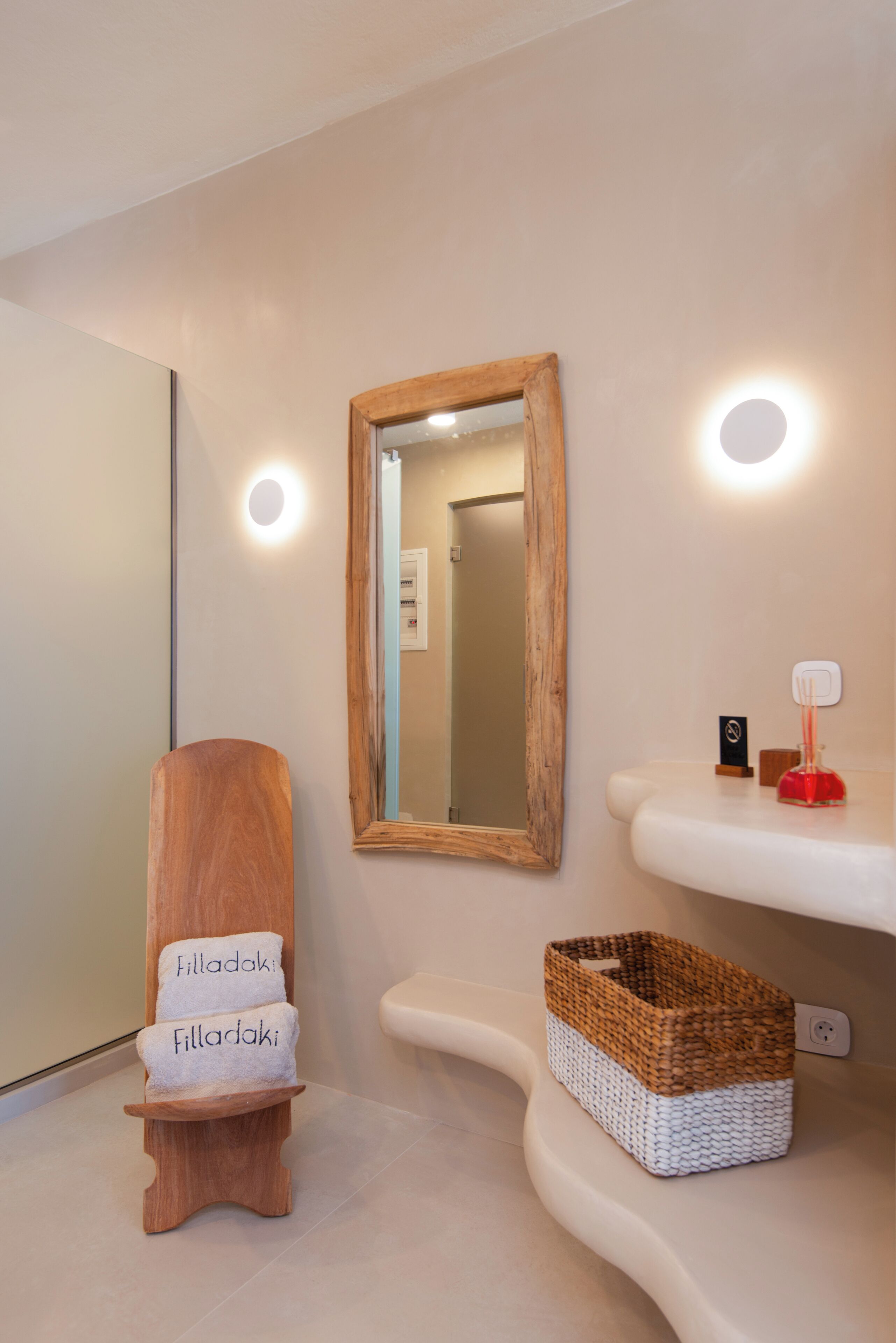 A bathroom with a wooden towel rack holding towels, a mirror, and a shelf with a basket and a soap dispenser.
