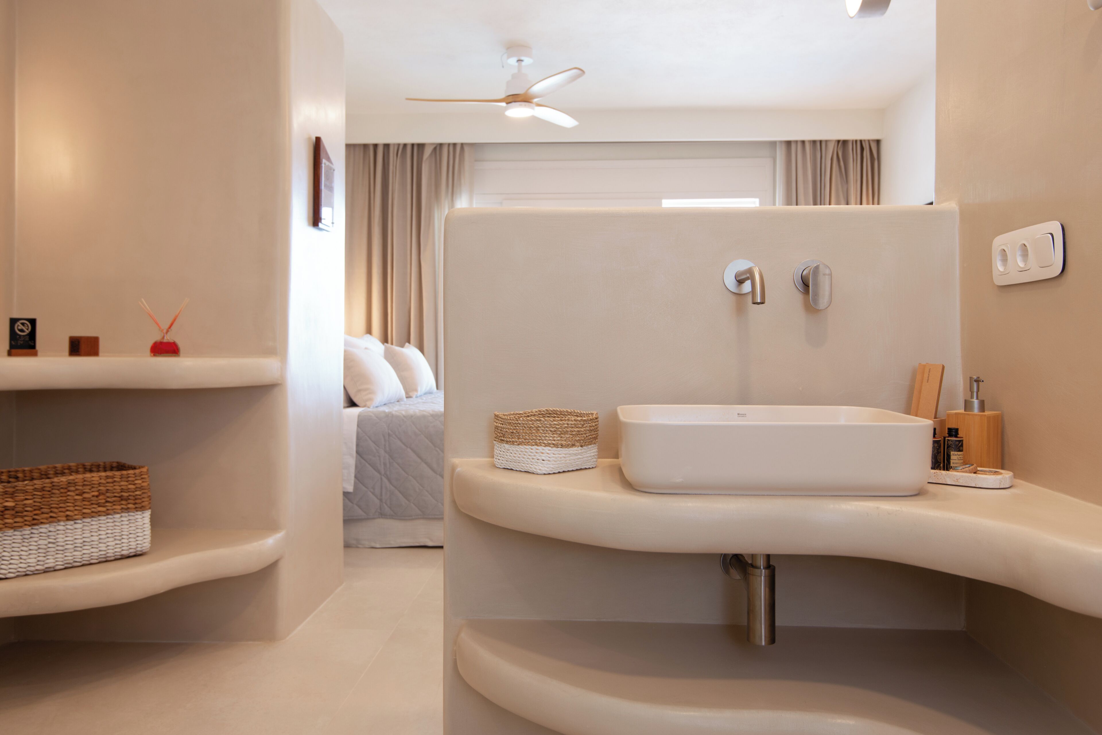 A modern bathroom with a freestanding sink, a ceiling fan, and a bedside table with a basket.