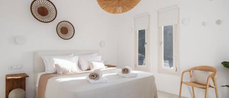 A minimalist bedroom with a large bed, two wall-mounted decorative items, a hanging light fixture, and a window with a view.