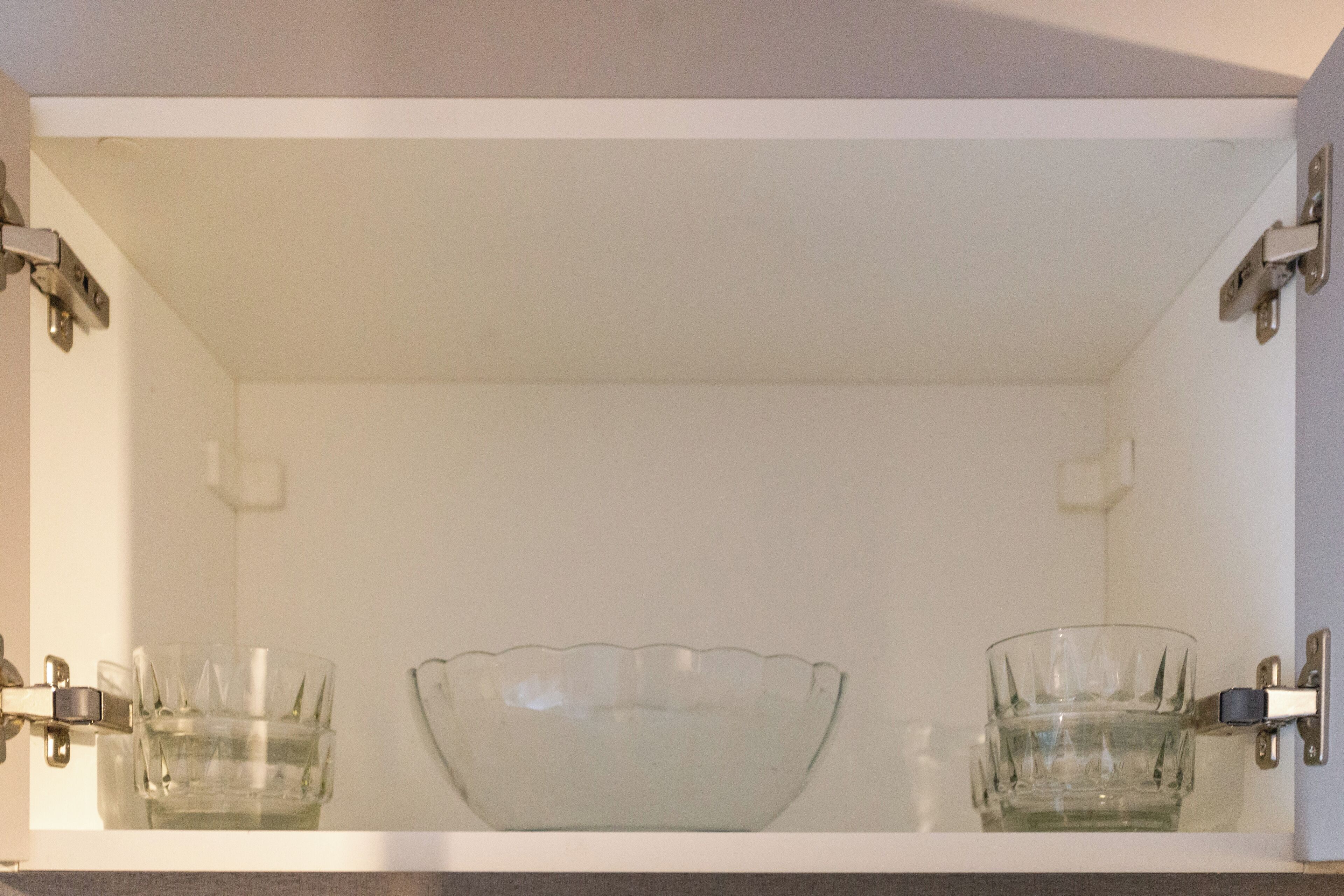 A white cabinet with two glass bowls and two glass cups.