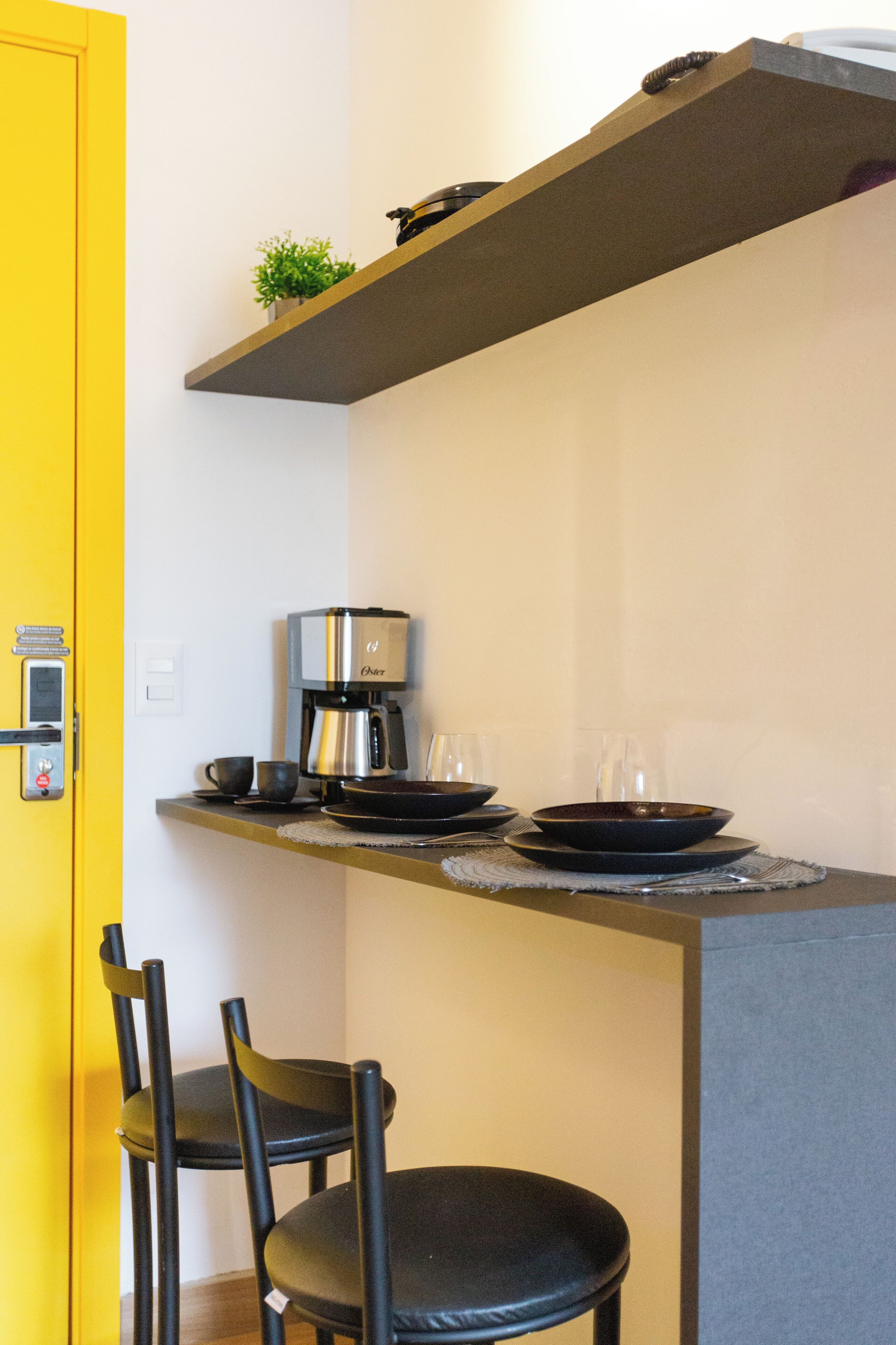 A compact kitchen with a coffee maker, two black plates, and a small plant on a shelf.