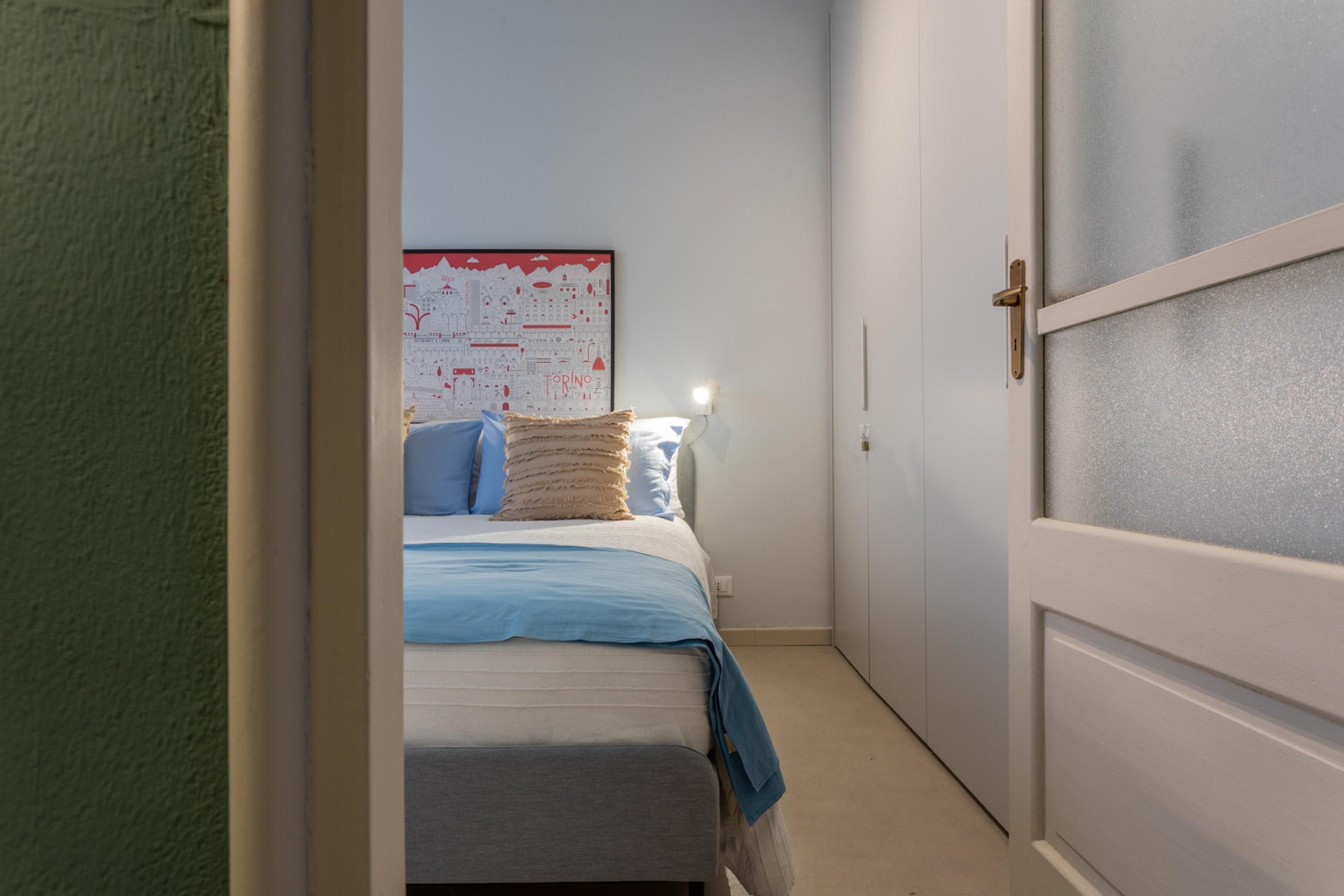 A narrow hallway leading to a bedroom with a bed, pillows, and a wall map.