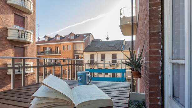 A wooden bench with an open book and a mug on it, a potted plant, and a blue bench in the background. - Casa Paradiso by Wonderful Italy (Turin)