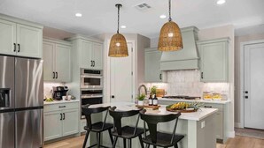 A modern kitchen with stainless steel appliances, light green cabinets, and a central island with bar stools. - Ohana Hive 5 Bedroom Townhouse (St. George)
