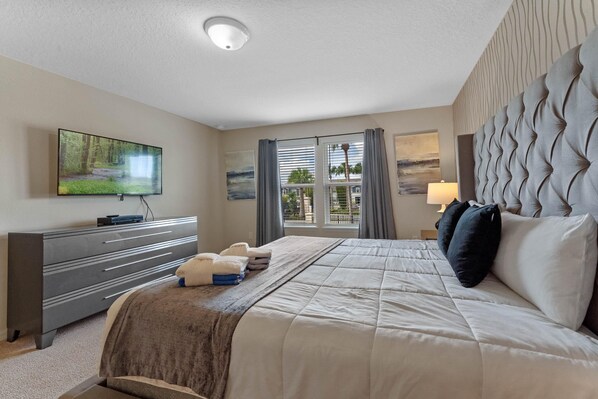 A hotel room with a large bed, a flat-screen TV mounted on the wall, a dresser, and a window with curtains.