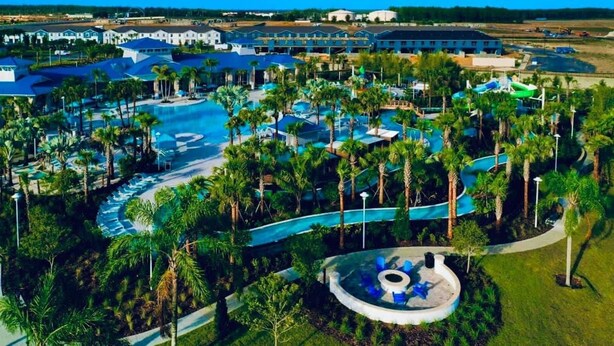 Luchtbeeld van een resort met meerdere zwembaden, palmbomen en een glijbaan.