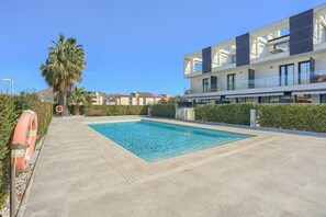 Un área de piscina moderna con piscina de agua cristalina, rodeada por un seto bajo y un flotador salvavidas.