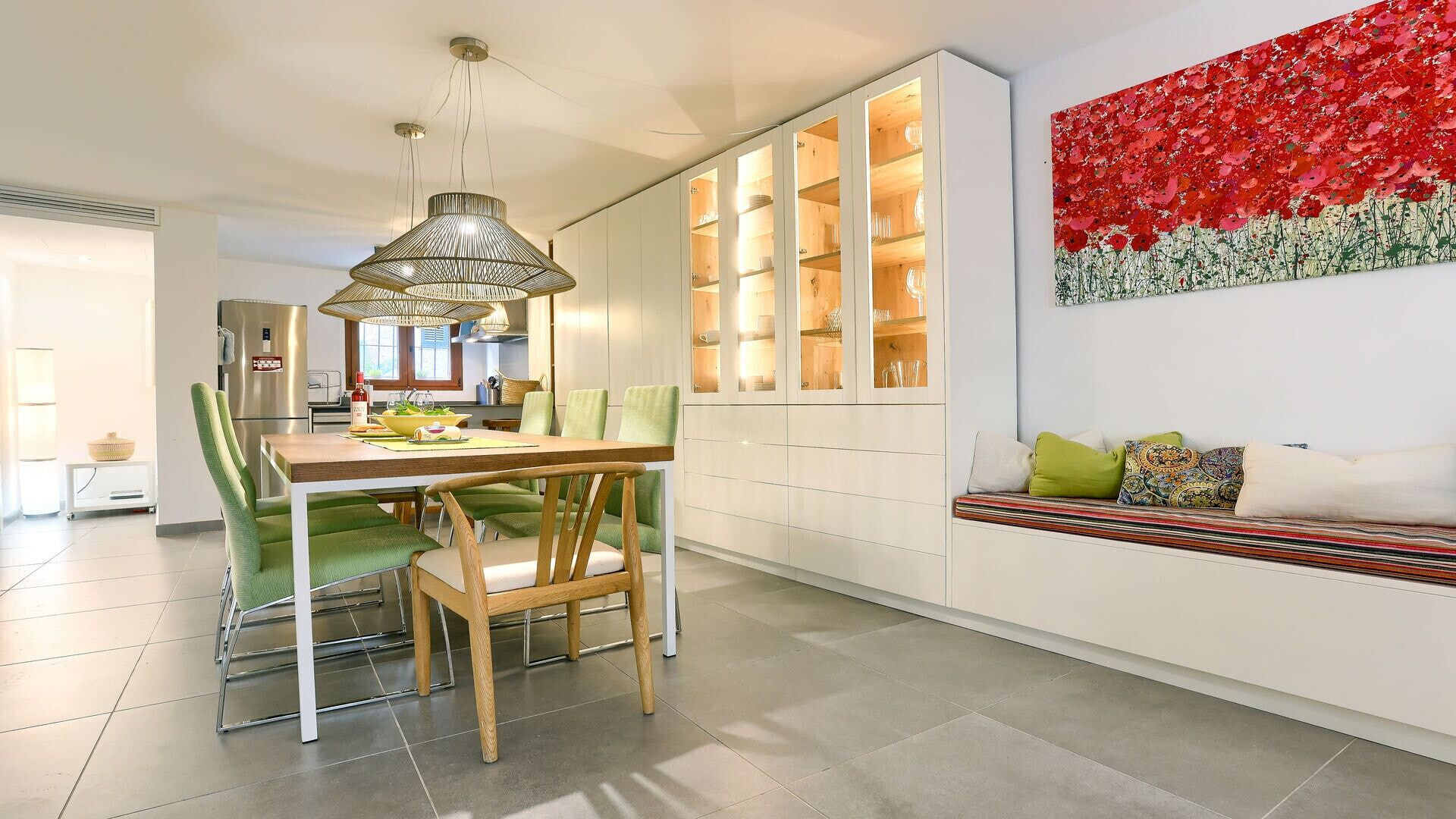 Una cocina moderna con comedor, que cuenta con una isla grande, sillas verdes y una llamativa obra de arte en la pared con colores rojo y verde.