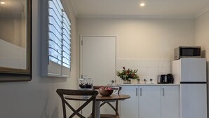 A modern kitchen with white cabinets, a refrigerator, a microwave, and a dining table with chairs. - Studio at Beechworth next to the forest. Pet friendly but please let us know. 
. (Beechworth)
