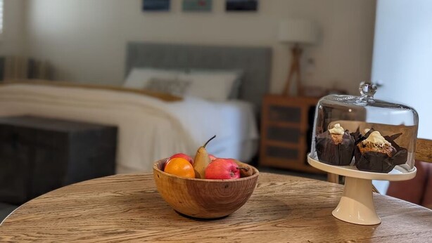 A wooden bowl with fruits and a cake on a table in a room with a bed and artwork on the wall. - Studio at Beechworth next to the forest. Pet friendly but please let us know. 
. (Beechworth)