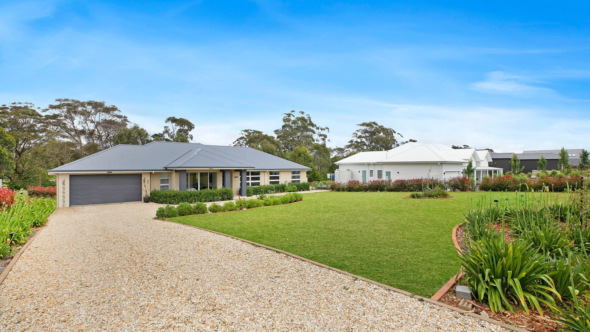 A residential property with a gravel driveway, a well-maintained lawn, and a variety of plants and shrubs.