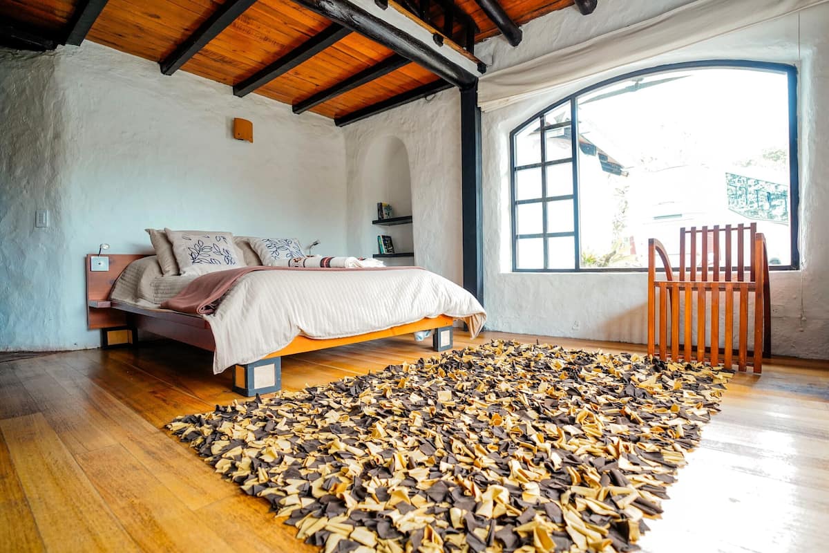 Ein Schlafzimmer mit Bett, Holzboden, großem Fenster und einem Stuhl.