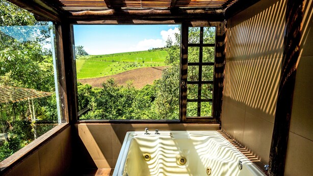 Une salle de bain dotée d’une grande baignoire, offrant une vue sur un paysage verdoyant par la fenêtre, et dont le plafond est orné de poutres en bois.