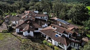 Un village traditionnel aux maisons aux toits de tuiles en terre cuite, entouré d’une végétation luxuriante et dominé par des montagnes en arrière-plan.