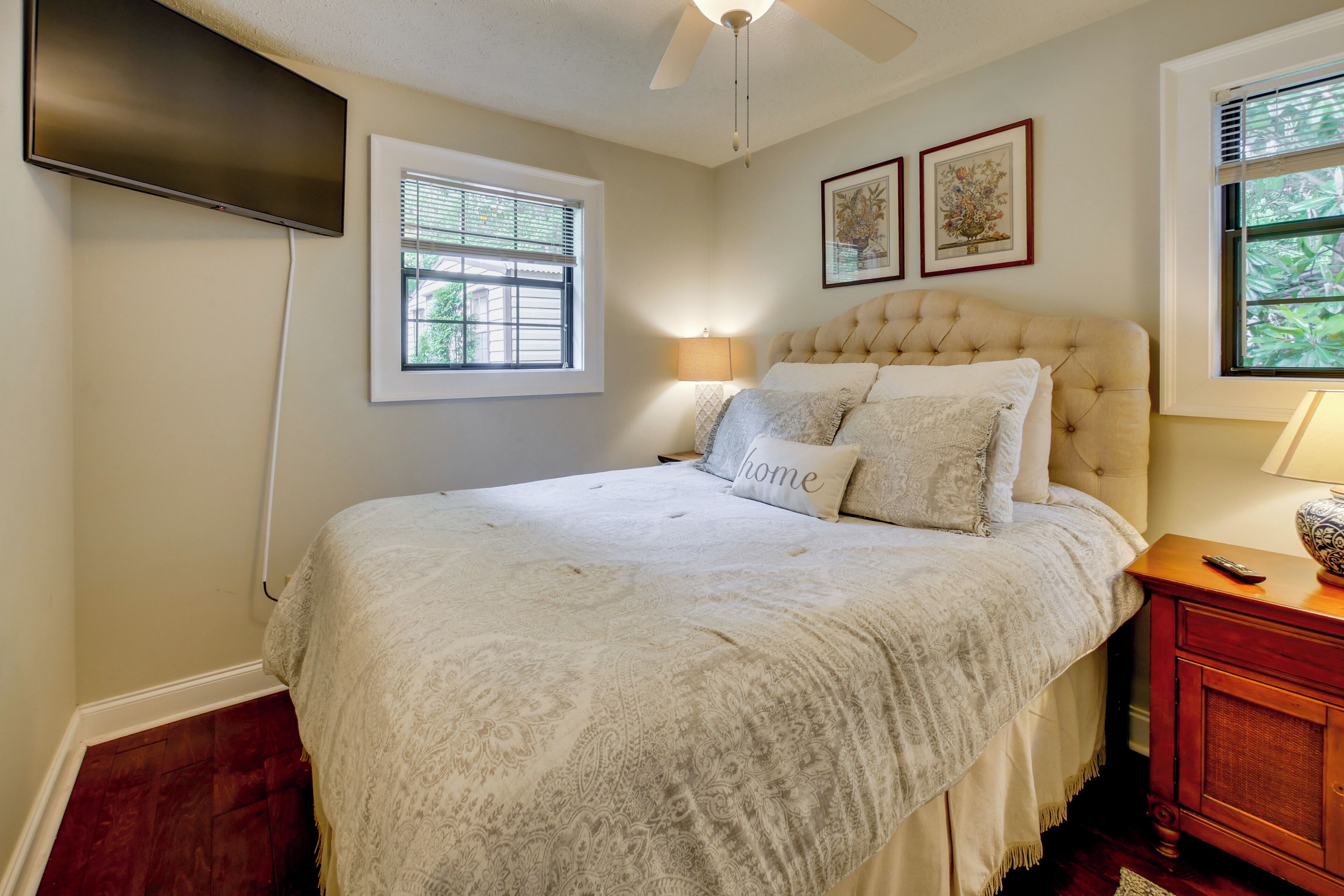 A bedroom with a bed, a ceiling fan, a TV mounted on the wall, and a window with blinds.