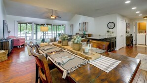 Un vaste espace dédié à la salle à manger, avec une table en bois, des chaises et une vue sur l’extérieur grâce à de grandes fenêtres.