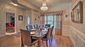 A dining room with a wooden table set for six, surrounded by chairs, a chandelier, and a large window with curtains. - Screened Patio: Rincon Home, 18 Mi to Savannah! (Rincon)