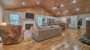 Un salon spacieux avec un plafond en bois, une cheminée, un canapé et un téléviseur.