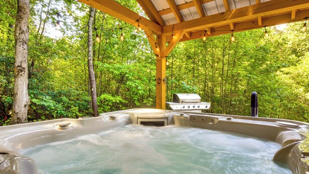Un bain à remous situé dans une zone boisée, surmonté d’une pergola en bois.
