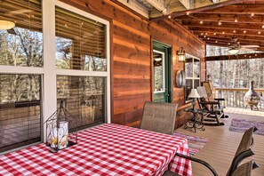 A wooden cabin with a covered porch, checkered table, wicker chairs, and a view of trees. - Stunning Blue Ridge Retreat w/ River Access! (Blue Ridge)