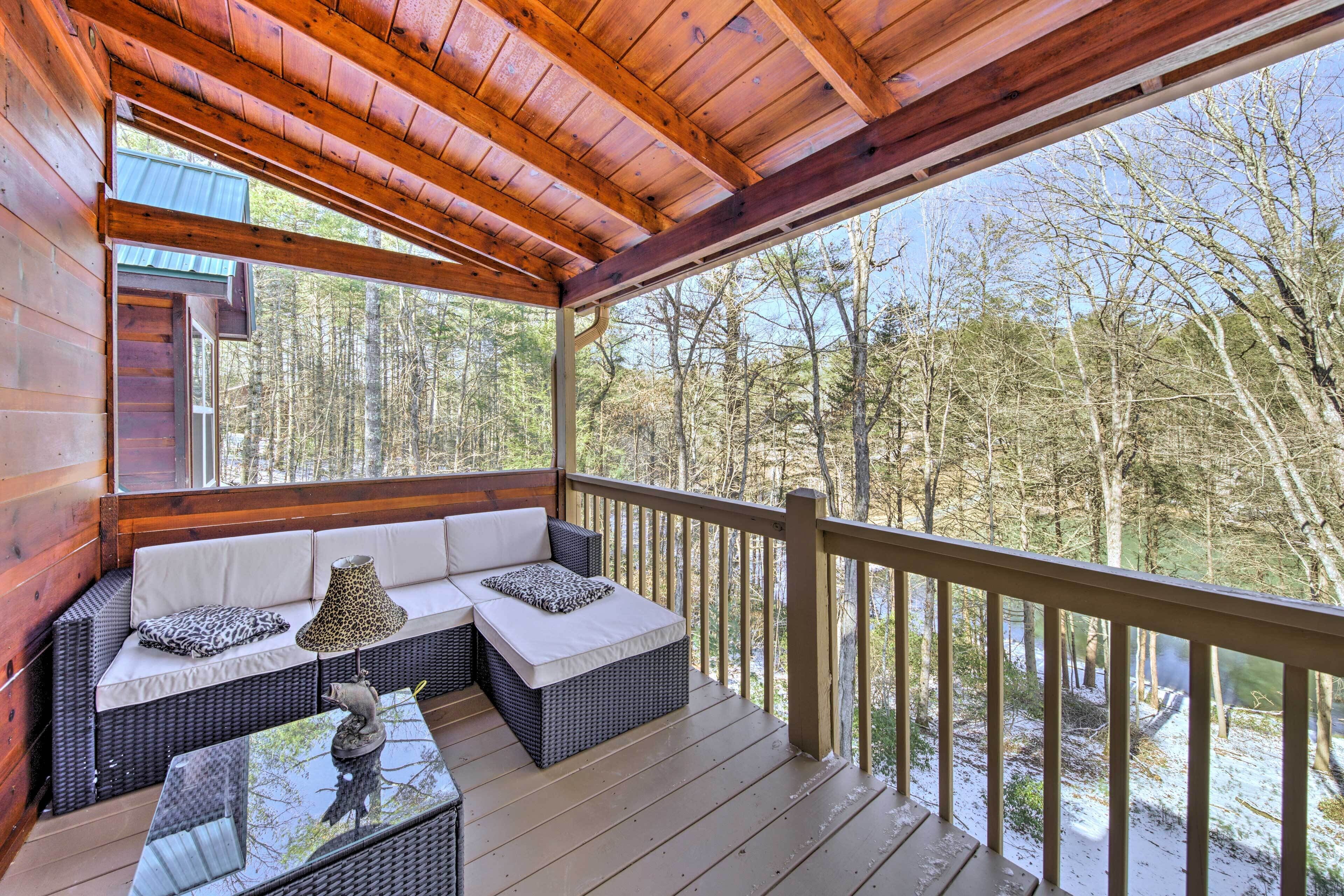 Une terrasse en bois avec un canapé et une table en verre, donnant sur une zone boisée.