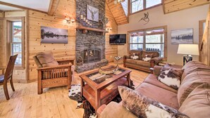A cozy log cabin interior with a stone fireplace, wooden furniture, and large windows. - Stunning Blue Ridge Retreat w/ River Access! (Blue Ridge)