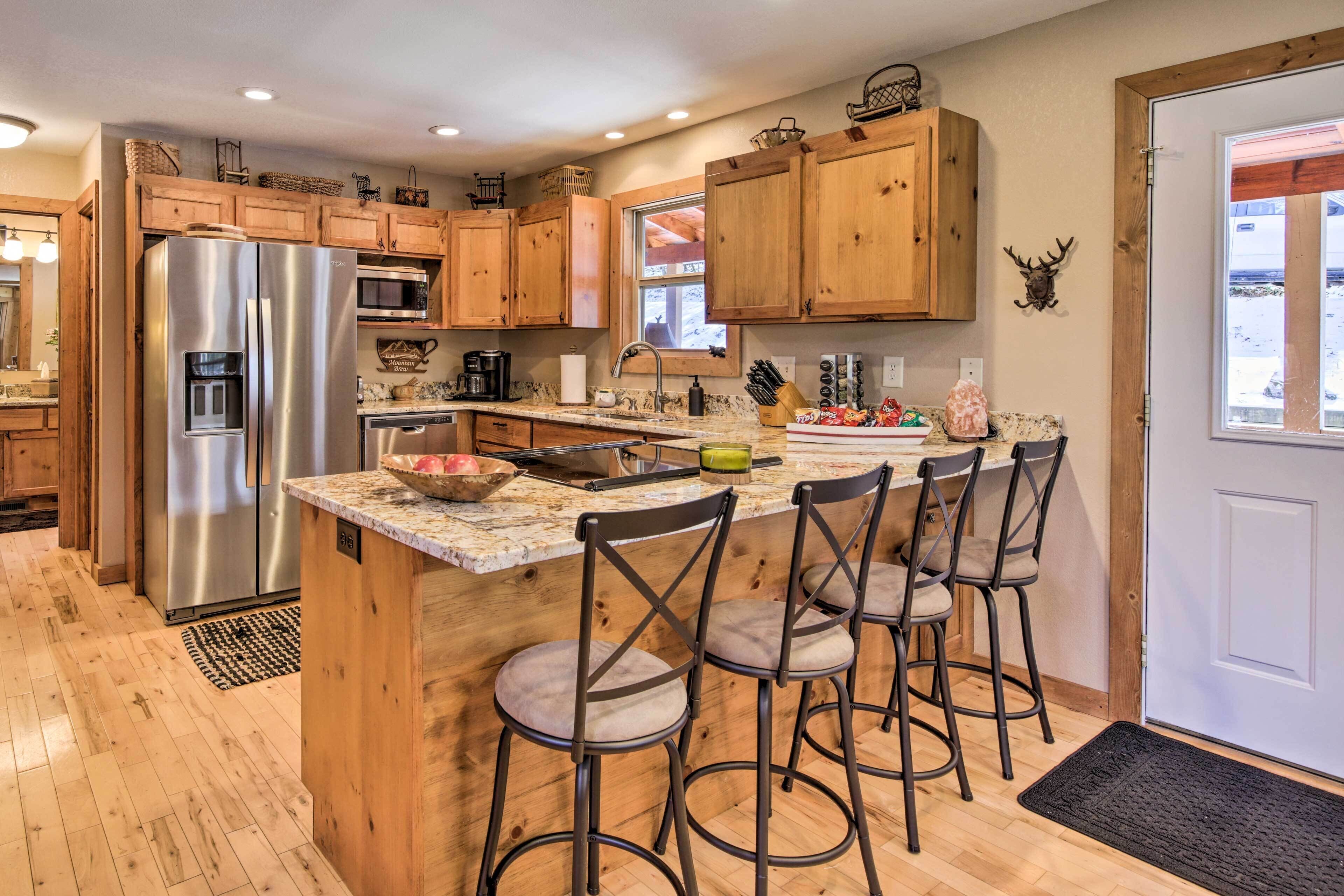 A kitchen with wooden cabinets, a stainless steel refrigerator, a marble countertop, and bar stools.