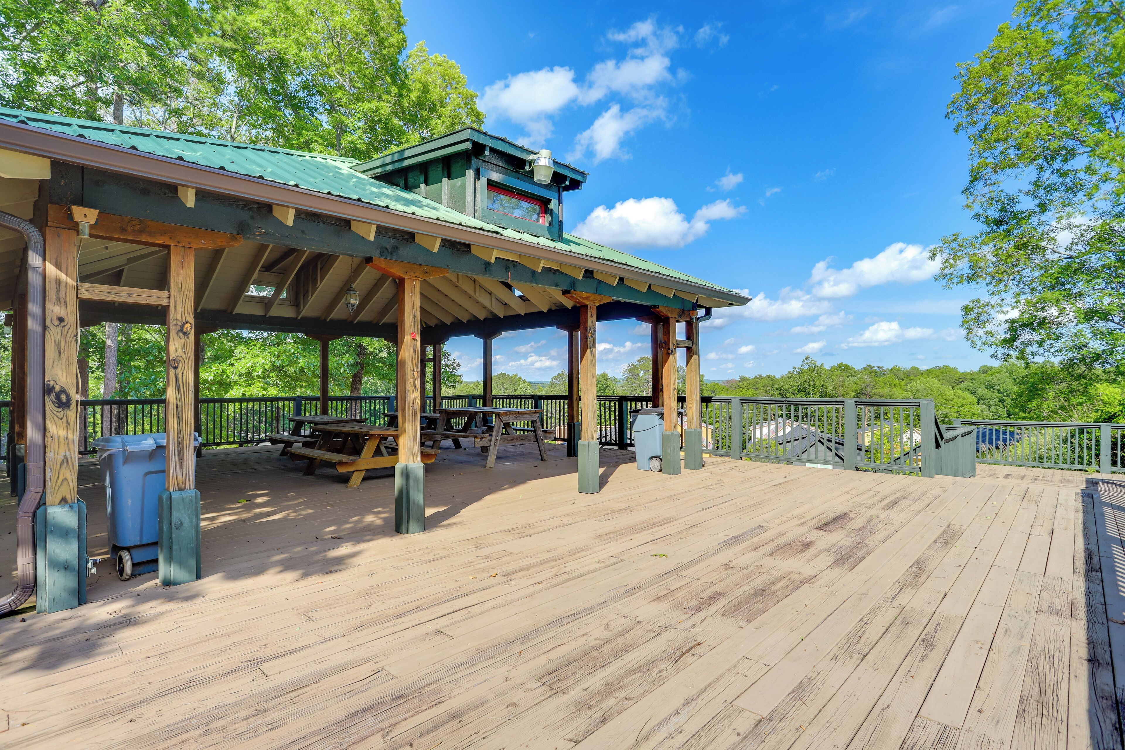 A wooden deck with a covered picnic area, picnic tables, and trash bins.
