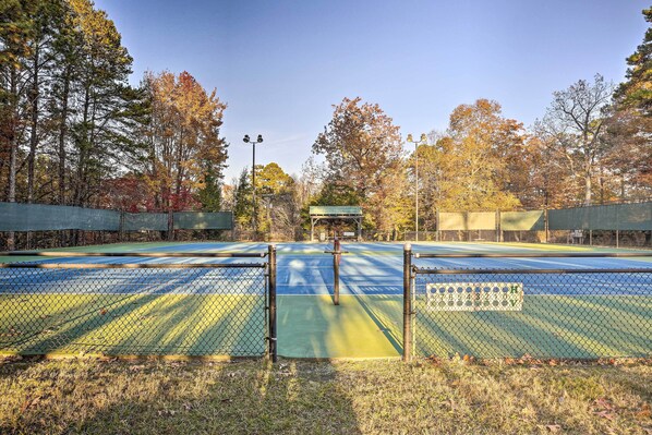 Un court de tennis entouré d  ’une clôture en treillis métallique, bordé d’arbres aux feuilles d’automne.