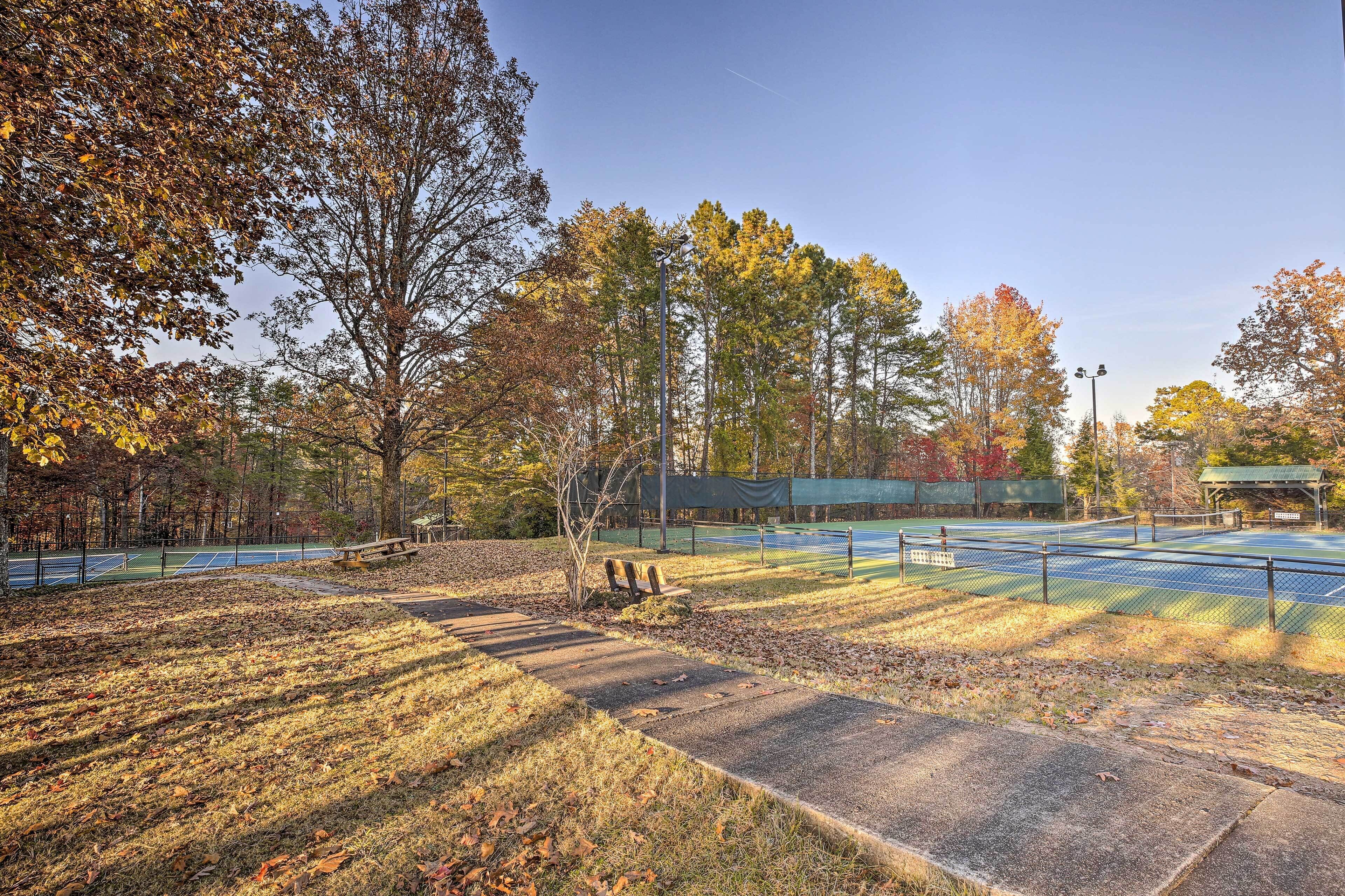 Una cancha de tenis al aire libre con árboles a su alrededor y una banca.