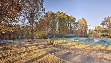 Una cancha de tenis al aire libre con árboles a su alrededor y una banca.