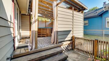 A wooden deck with a bench, a covered area with string lights, and a blue house in the background.