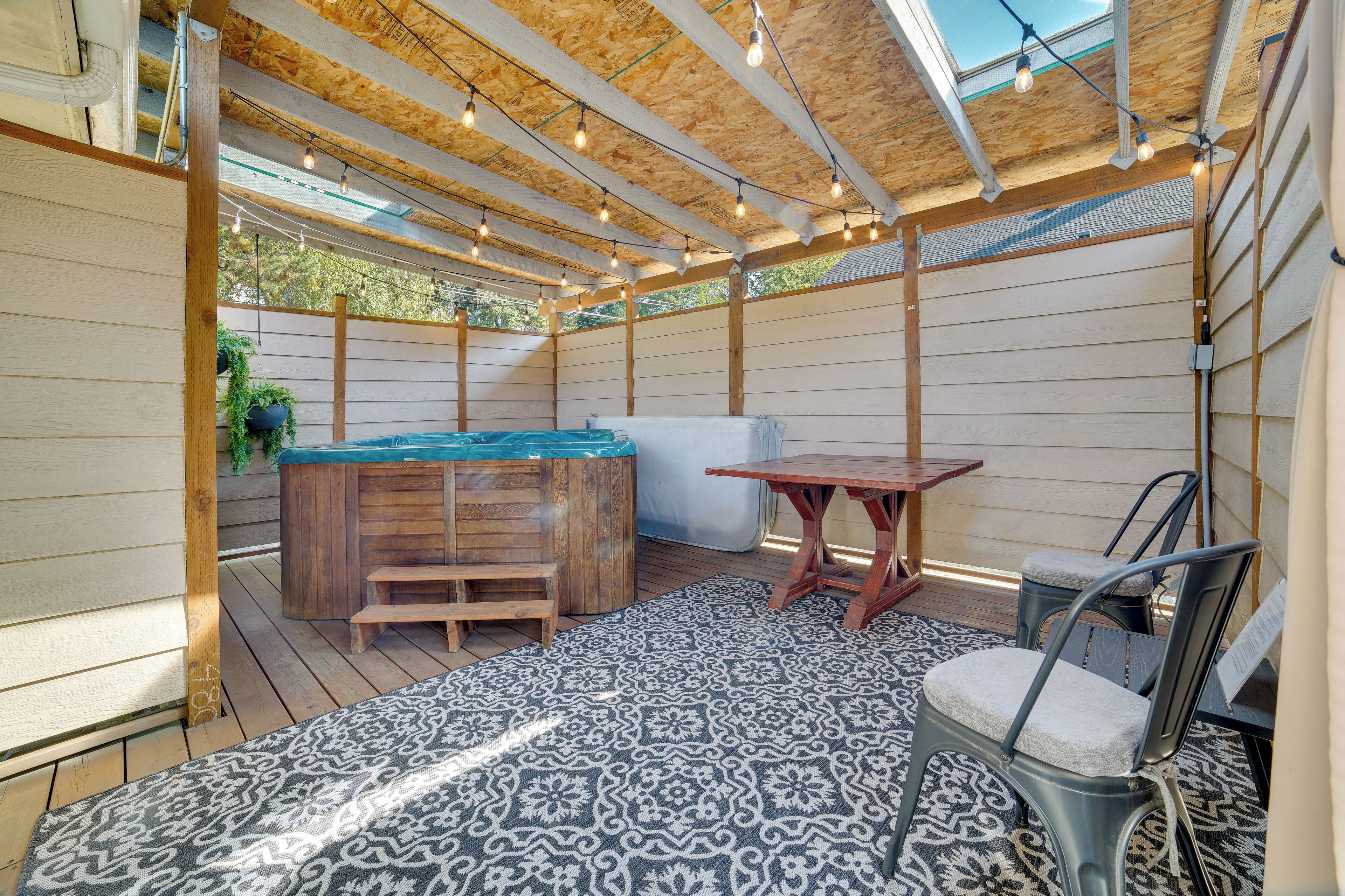 Un espacio exterior cubierto con terraza de madera, jacuzzi, mesa y sillas.